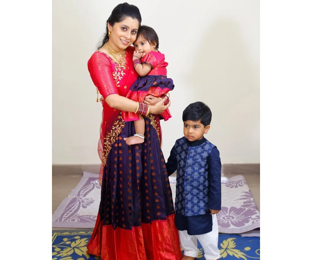 Here is a wonderful example of how I create coordinated outfits for the whole family. The mother and daughter are twinning in a custom red and blue silk lehenga set, while the son wears a complementary blue brocade kurta, ensuring everyone looks connected and stylish.