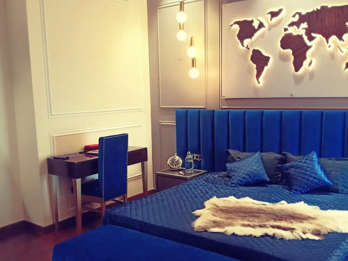 A striking modern bedroom centered around a royal blue velvet bed. The design includes a matching tufted bench, a minimalist study desk, and a custom backlit world map art piece on the wall, creating a bold and personalized travel-themed sanctuary.