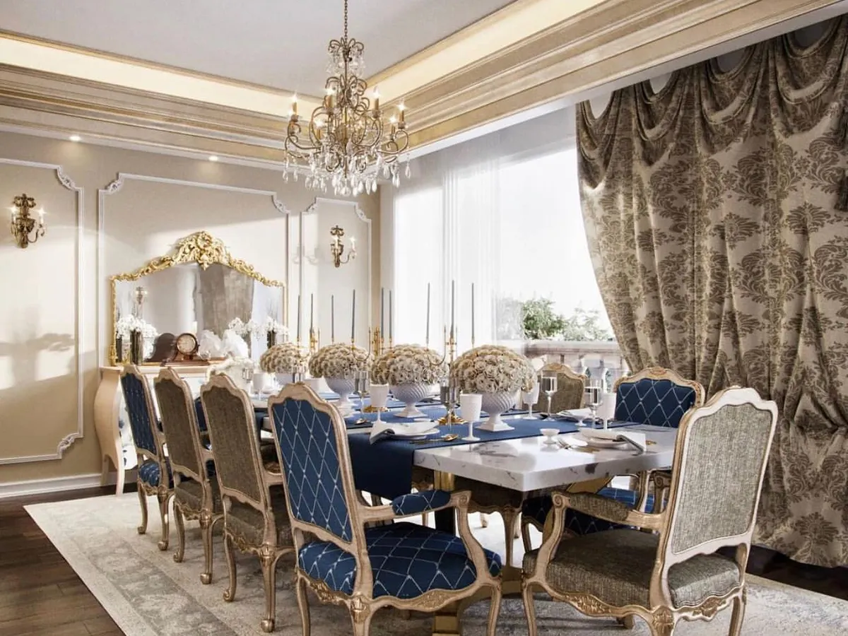 We designed this dining area to be the heart of a timeless, classical residence. The space is defined by its opulence, featuring custom chairs with intricate woodwork, a crystal chandelier, and heavy, patterned drapes that control natural light. The design amplifies the vintage character of the home, creating an elegant setting for formal gatherings.