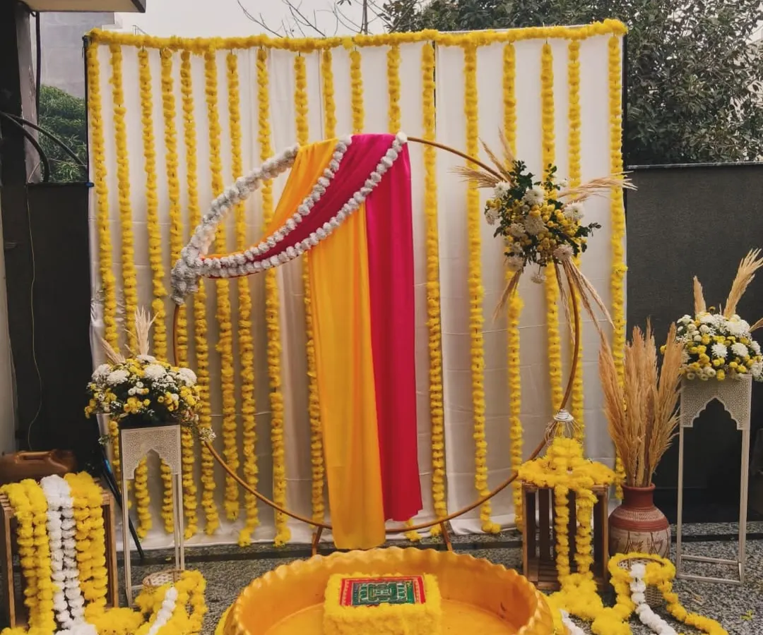 For this Haldi ceremony, I designed a setup that blends tradition with modern elegance. The backdrop features strings of vibrant marigolds, while the seating area is defined by a beautiful urli, all framed by a contemporary golden ring draped in rani pink and yellow fabric.