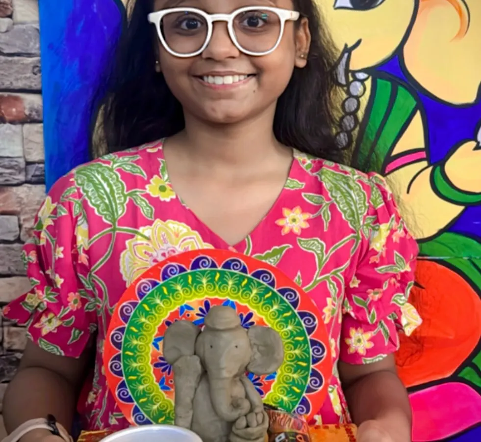 I love seeing the pride on a child's face when they complete their masterpiece. Here, a young artist proudly displays her handmade clay Ganesha idol, sculpted and decorated during our festive workshop. This is a great example of our hands-on clay modeling sessions for kids.