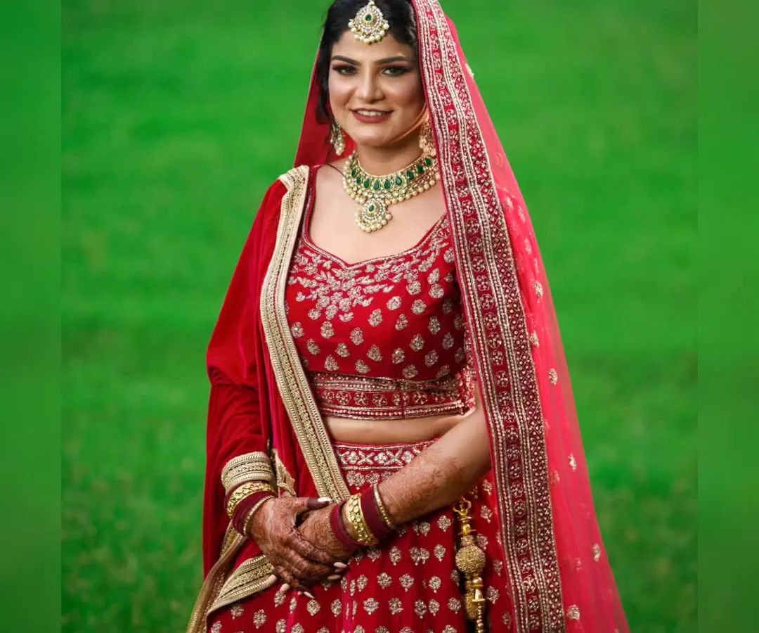 A classic bridal portrait of a bride in a stunning red lehenga, set against a vibrant green backdrop. I focused on creating a timeless image that highlights her elegance and the rich details of her wedding attire.