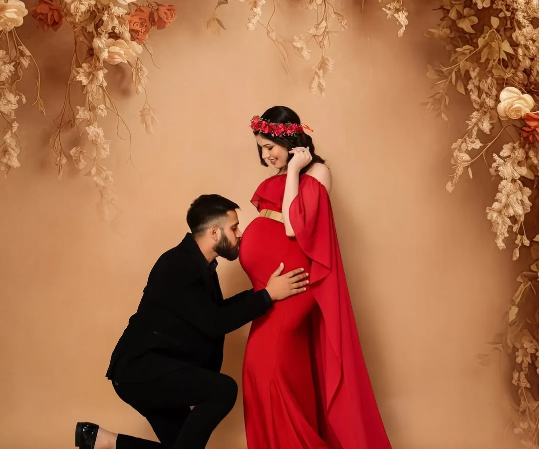 A dramatic and elegant maternity portrait. The striking contrast of the flowing red gown against a fine art, neutral-toned backdrop creates a powerful, celebratory image. This style is perfect for parents who want a bold and artistic commemoration of their pregnancy journey.