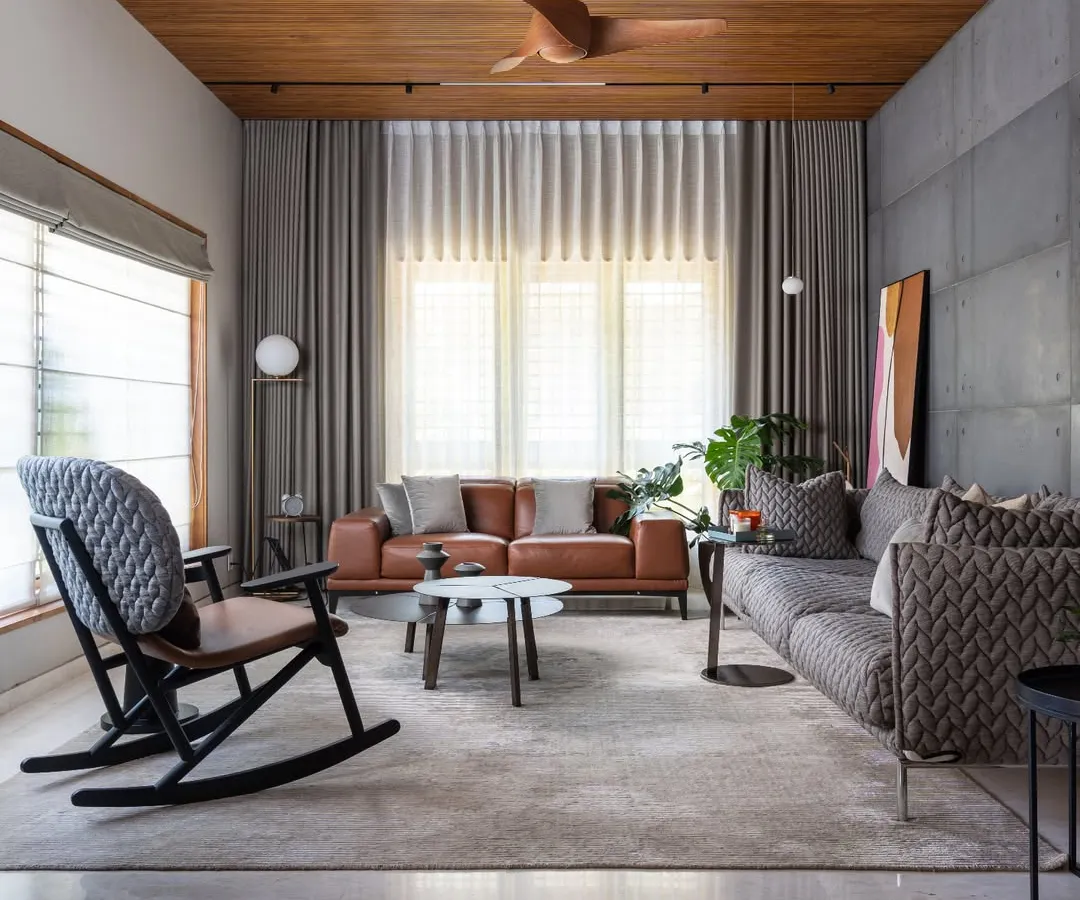 A living room from our Faizal Residence project, designed for comfort and conversation. We combined a plush patterned sofa with a classic leather couch and a modern rocking chair, all set against a backdrop of exposed concrete and warm wood ceilings to create a space that is both sophisticated and welcoming.