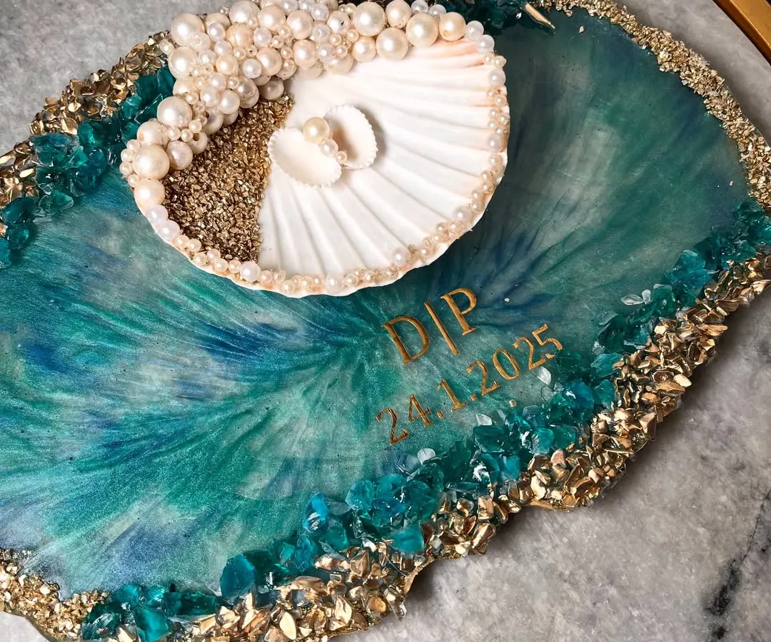 For the couple that loves the sea, I designed this unique ocean-themed ring platter. It features swirling teal and blue resin that mimics ocean waves, a real seashell ring holder adorned with pearls, and a border of sand and crystals. I can personalize it with your initials and special date.