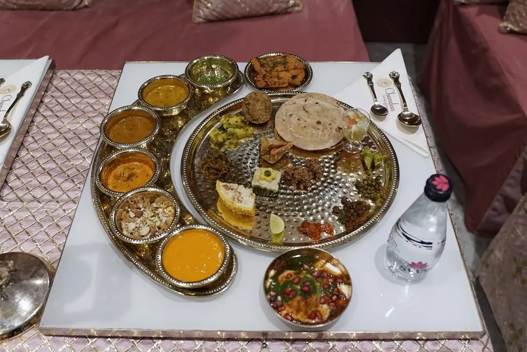 A traditional Rajasthani thali, served with royal treatment. This sit-down meal features an array of authentic dishes, from dal and bati to various sabzis and sweets, presented in classic silverware.