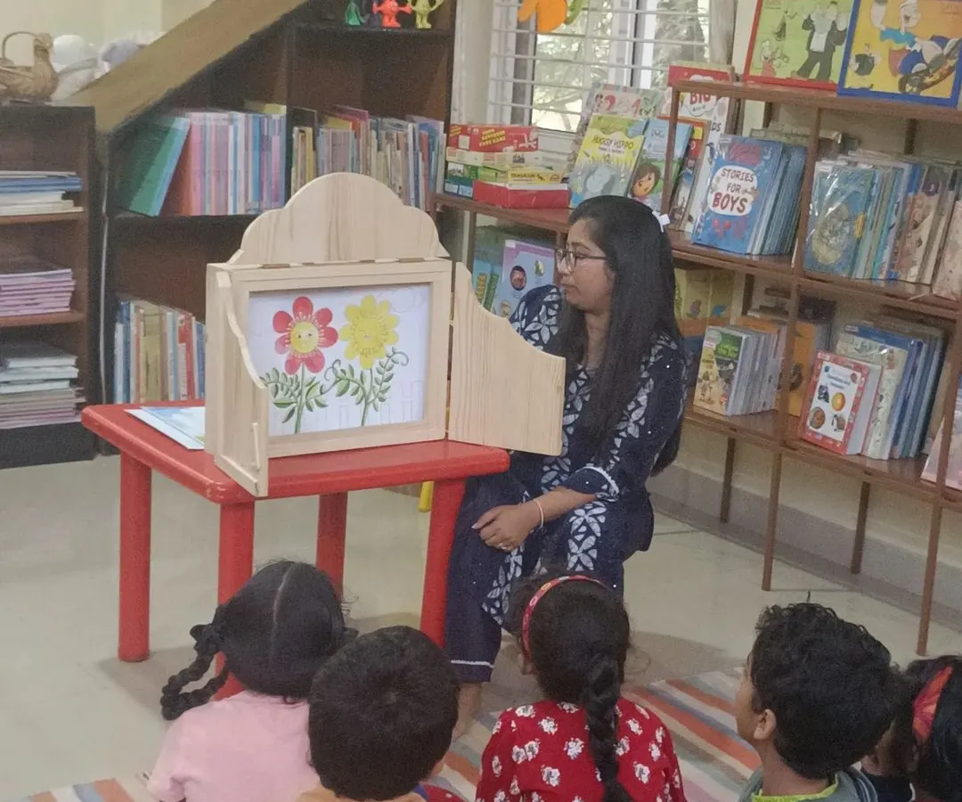 We use special tools like this traditional wooden puppet stage to make stories even more magical. Here, children are captivated as illustrations come to life, drawing them deeper into the narrative.