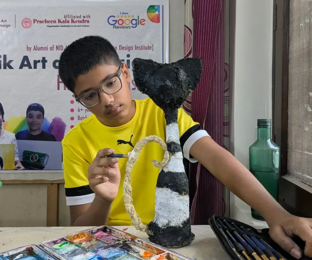 It's all about the process. Here, a young artist is completely absorbed in painting the final details on his papermache cat sculpture, learning patience and precision along the way.