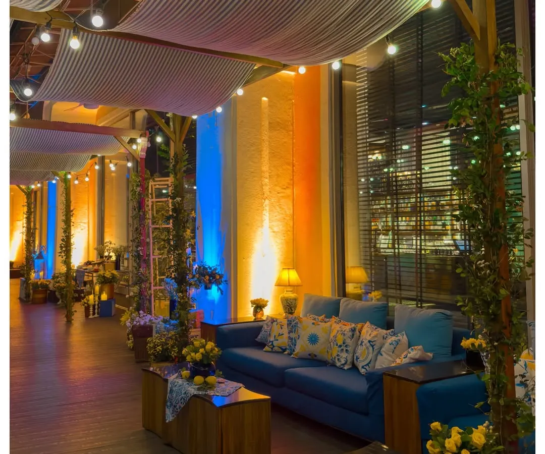 I transformed this indoor venue into a breezy Sicilian veranda. By installing a pergola with draped fabric and string lights, and using a mix of warm and cool uplighting, I created distinct zones for lounging and socializing that felt both expansive and intimate.