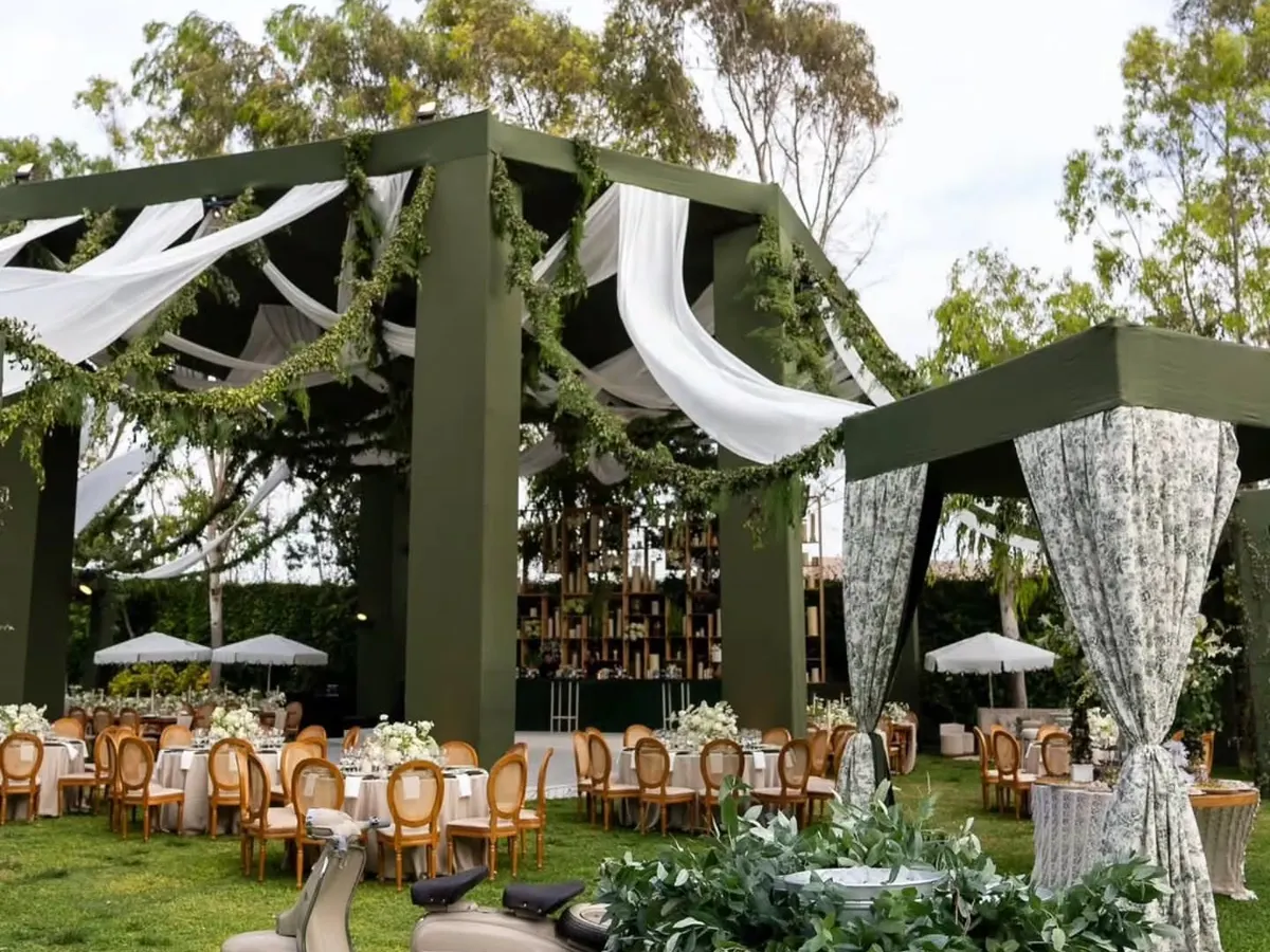 For this elegant 50th anniversary, I created a sophisticated green and white haven. This wide view shows the custom-built structures, flowing drapes, and relaxed seating areas that transformed a simple lawn into a luxurious outdoor venue.