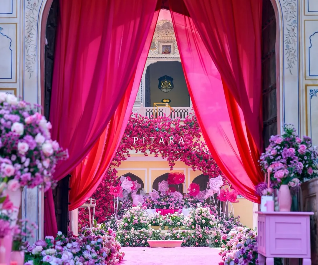 This is how we do royal entrances. A vibrant gulabi carpet and lush floral arrangements guide guests through majestic palace arches, framed by dramatic fuchsia drapes. It’s a welcome that promises the grandeur to come.