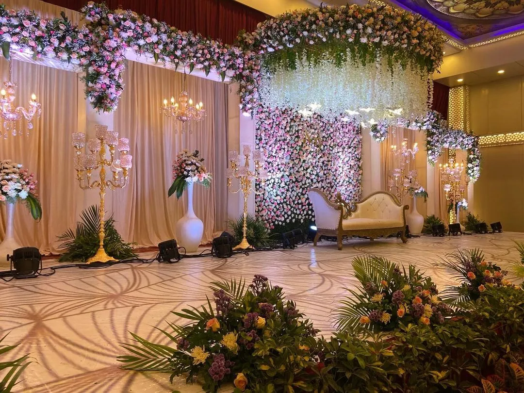 A vision of modern romance, this reception stage combines a massive floral wall, a cascading ceiling of white wisteria, and elegant lounge seating. We design spaces that feel both grand and intimately personal.