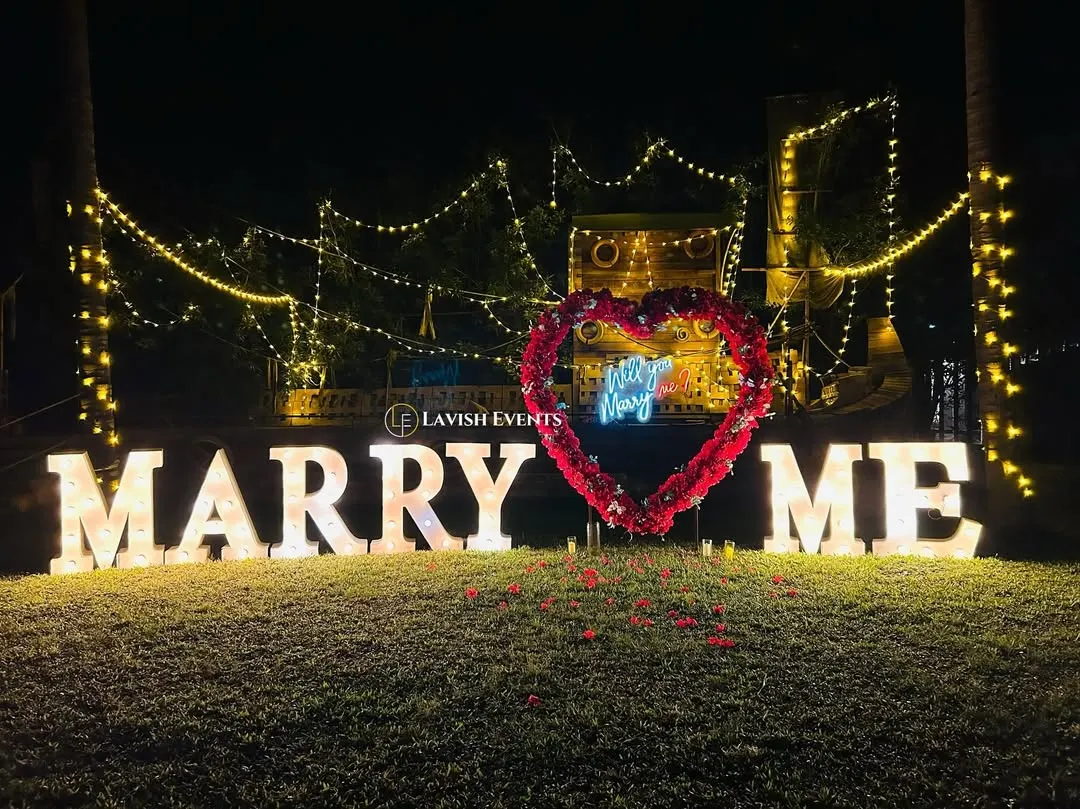Setting the stage for a 'yes'. This romantic proposal setup with giant marquee letters and fairy lights is all about creating that magical moment you've always dreamed of.
