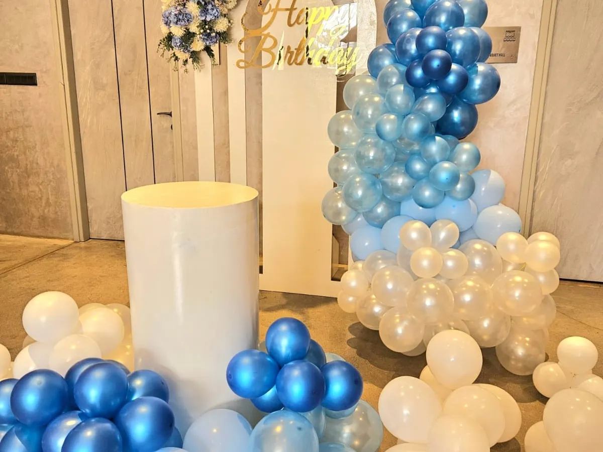 For a stylish 12th birthday, we designed this modern and chic setup. It features a cool blue and white balloon arrangement, a layered arch backdrop, and clean white plinths for a sophisticated party look.