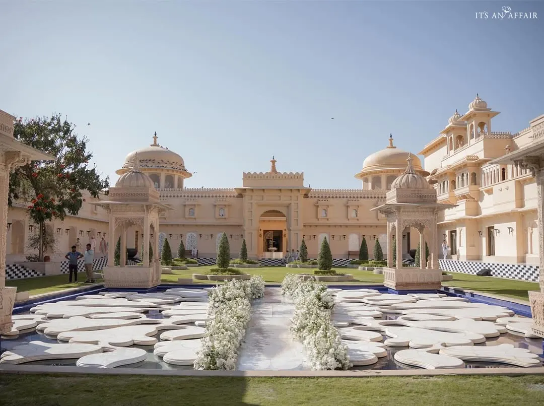 A breathtaking Anand Karaj ceremony at The Oberoi Udaivilas. The aisle, lined with pristine white florals, leads to a serene water body, perfectly framing the majestic palace architecture for this destination wedding in Udaipur.