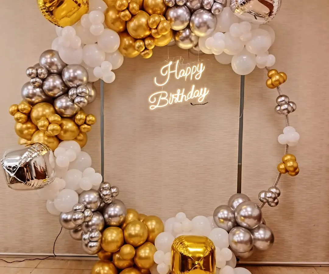 For a modern and chic birthday celebration, I design statement pieces like this circular frame with a custom 'Happy Birthday' neon sign. The organic balloon garland in gold, silver, and white adds a touch of elegance and is perfect for photos.