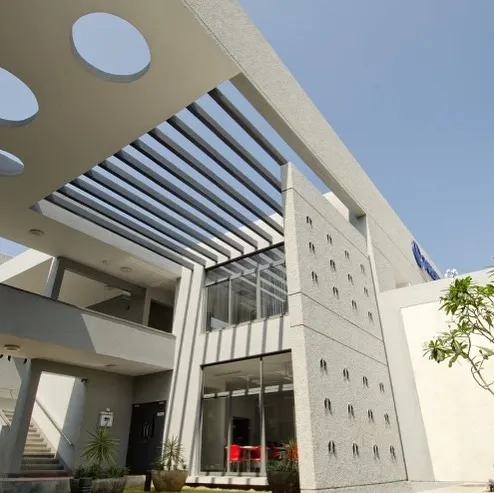 An exterior view of the Torishima Pumps corporate campus in Hosakote. We designed the building with clean geometric lines, using textured concrete and a slatted pergola to create dynamic patterns of light and shadow. This approach demonstrates our focus on creating visually engaging facades in commercial architecture.