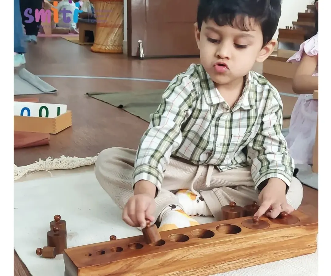 A child shows deep concentration while working with the Montessori knobbed cylinder block. This sensorial activity helps refine his visual discrimination of size and prepares him for writing by strengthening his pincer grip.