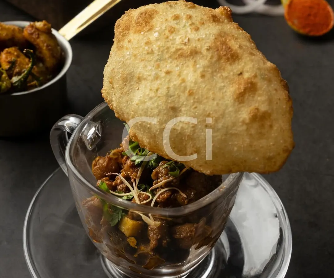 A modern interpretation of a beloved classic, our Chole Bhature. We serve the spiced chickpea curry in a glass cup, topped with a single, perfectly puffed bhatura, transforming a traditional dish into a chic, single-serving experience.