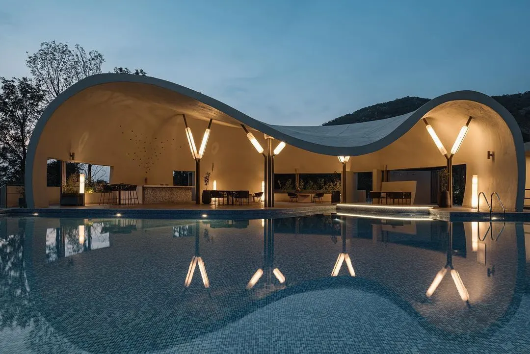 This is the Aqua Pool & Spa, a modern cave-like structure designed to celebrate the surrounding hills. The evening view highlights the custom lighting which reflects in the water, creating a tranquil and immersive atmosphere that blends architecture with the natural landscape.