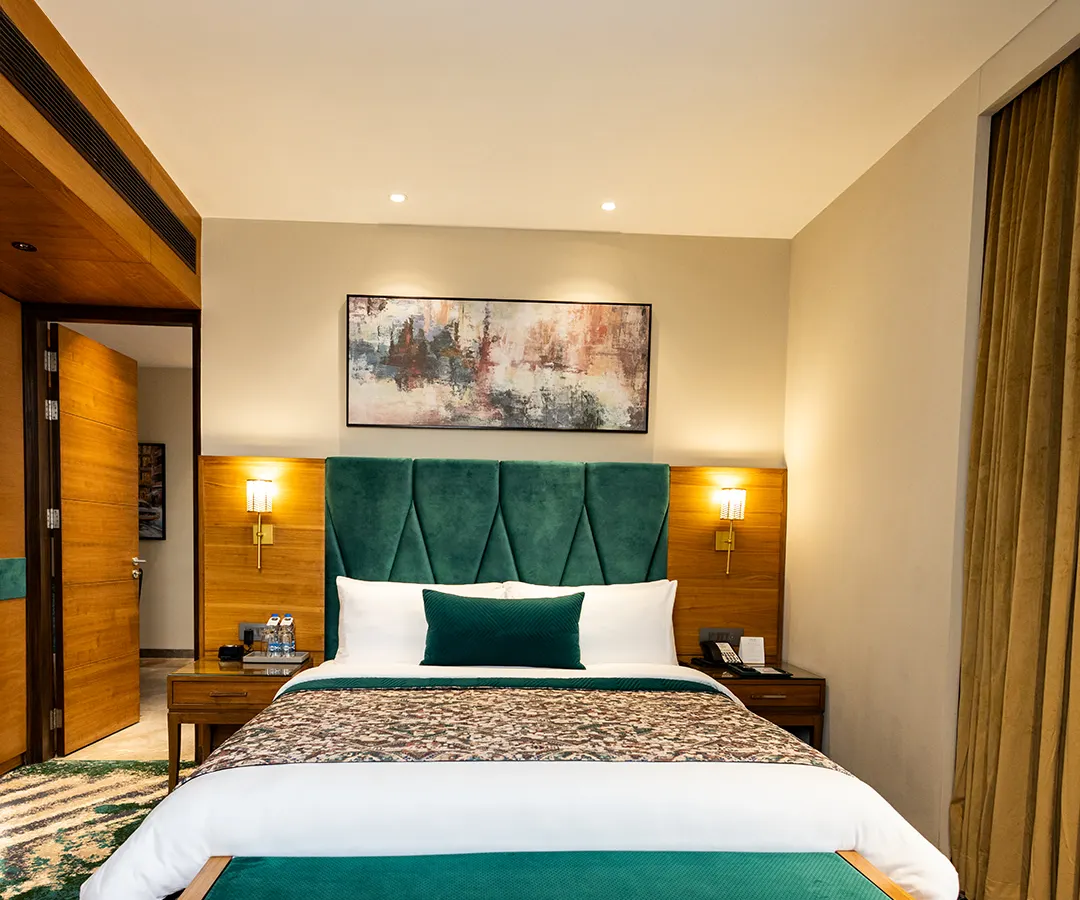 This is our deluxe room, featuring a plush, king-sized bed with an elegant emerald green headboard. It’s a space designed for deep rest and rejuvenation after a day in the city.