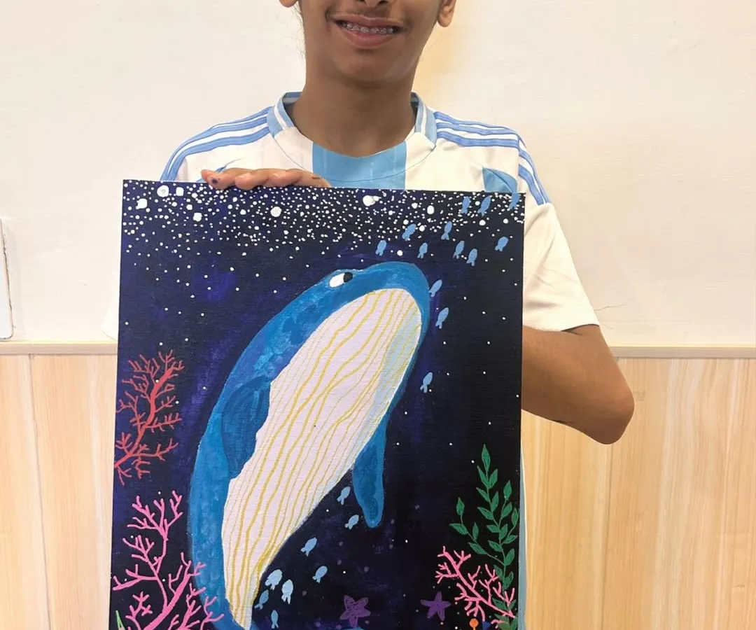 Look at that proud smile! This is the result of our personalized canvas painting sessions. I guide each student to bring their vision to life, like this incredible underwater whale scene, teaching them acrylic painting techniques while they have a blast creating their own masterpiece.