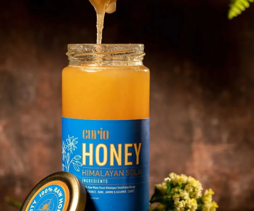 Capturing the rich texture of Himalayan honey required careful lighting to showcase its viscosity as it drips from the dipper. The natural wood and floral elements in the background reinforce the product's pure and organic origins.