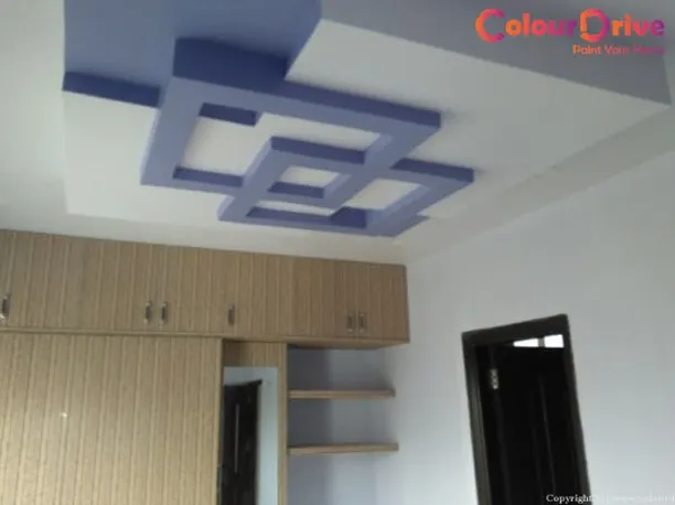 We created a bold statement in this bedroom with a custom geometric false ceiling. The intersecting blue and white POP structures add a modern, artistic touch and visual interest to the room, complementing the wooden cabinetry below.