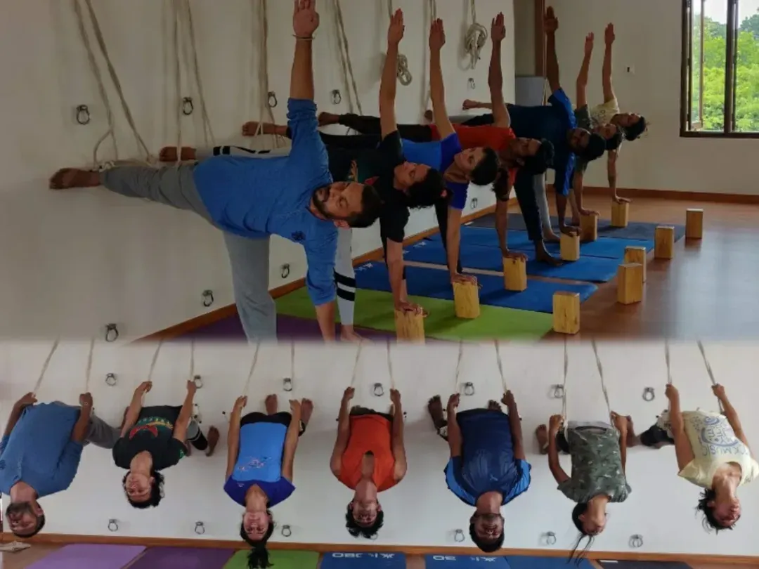 Our shala is a space for growth and community. Here, students engage in Ardha Chandrasana using blocks for alignment and explore inversions with the safety of the rope wall. This image captures the essence of our training: foundational learning supported by props and the exploration of advanced techniques.