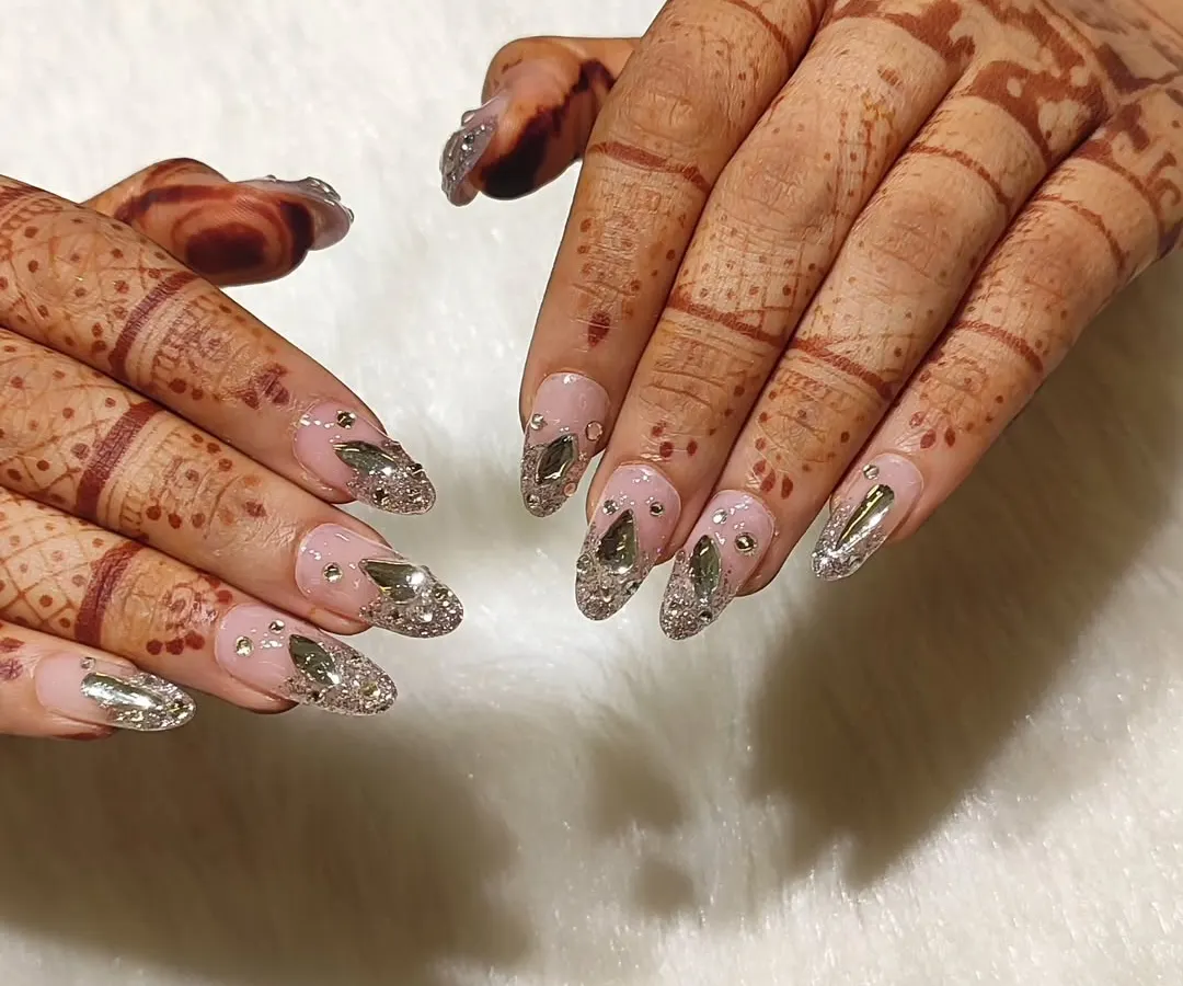 For the bride who wants to be the main character. This wedding nail set features a sheer pink base with a cascade of silver glitter and hand-placed, multi-faceted crystals for maximum sparkle that complements your mehendi.
