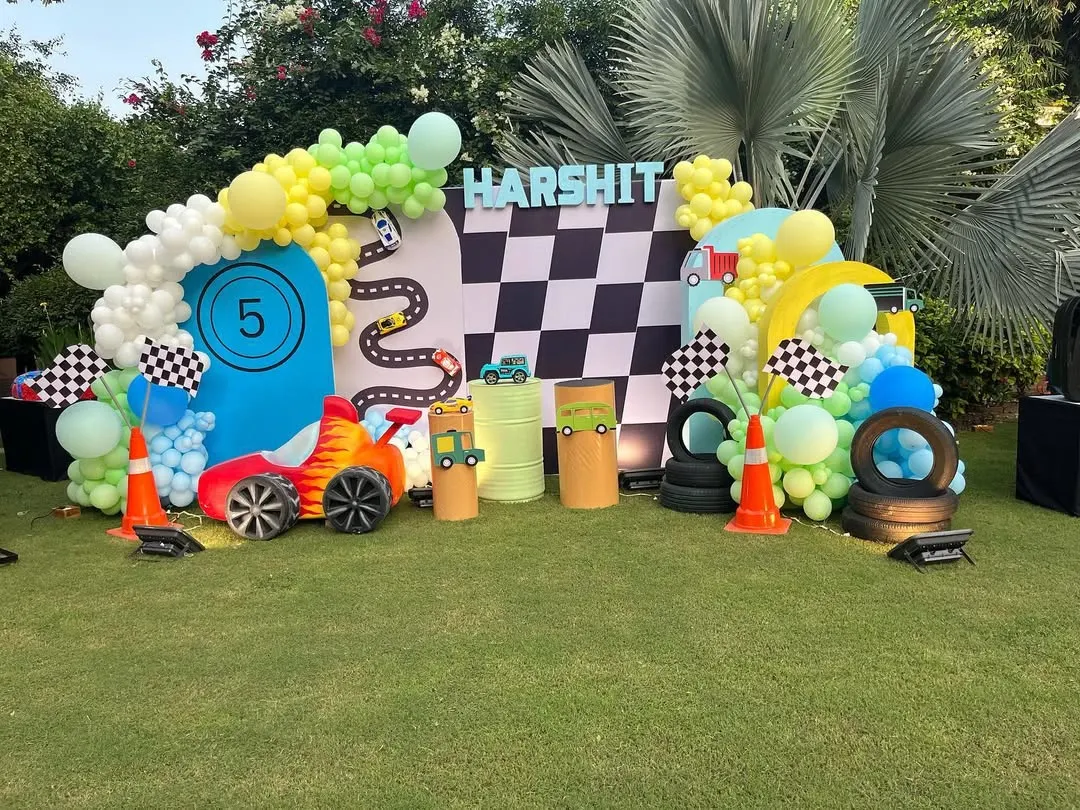 I created this action-packed car race theme for a 5th birthday party in a garden setting. The setup includes a checkered flag backdrop, custom racetrack cutouts, tire props, and a vibrant balloon arch in green, yellow, and blue.