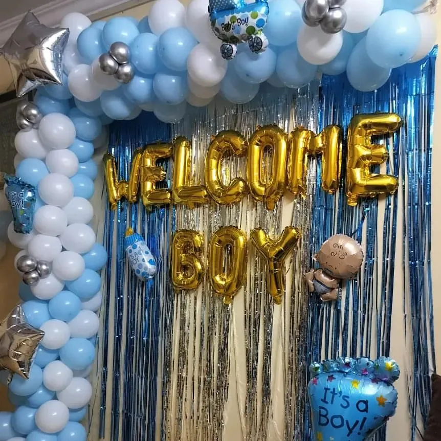 This is my classic "Welcome Boy" decoration, perfect for celebrating the arrival of a baby boy. The design includes a blue, white, and silver balloon arch complemented by a silver tinsel backdrop and cute baby-themed foil balloons.