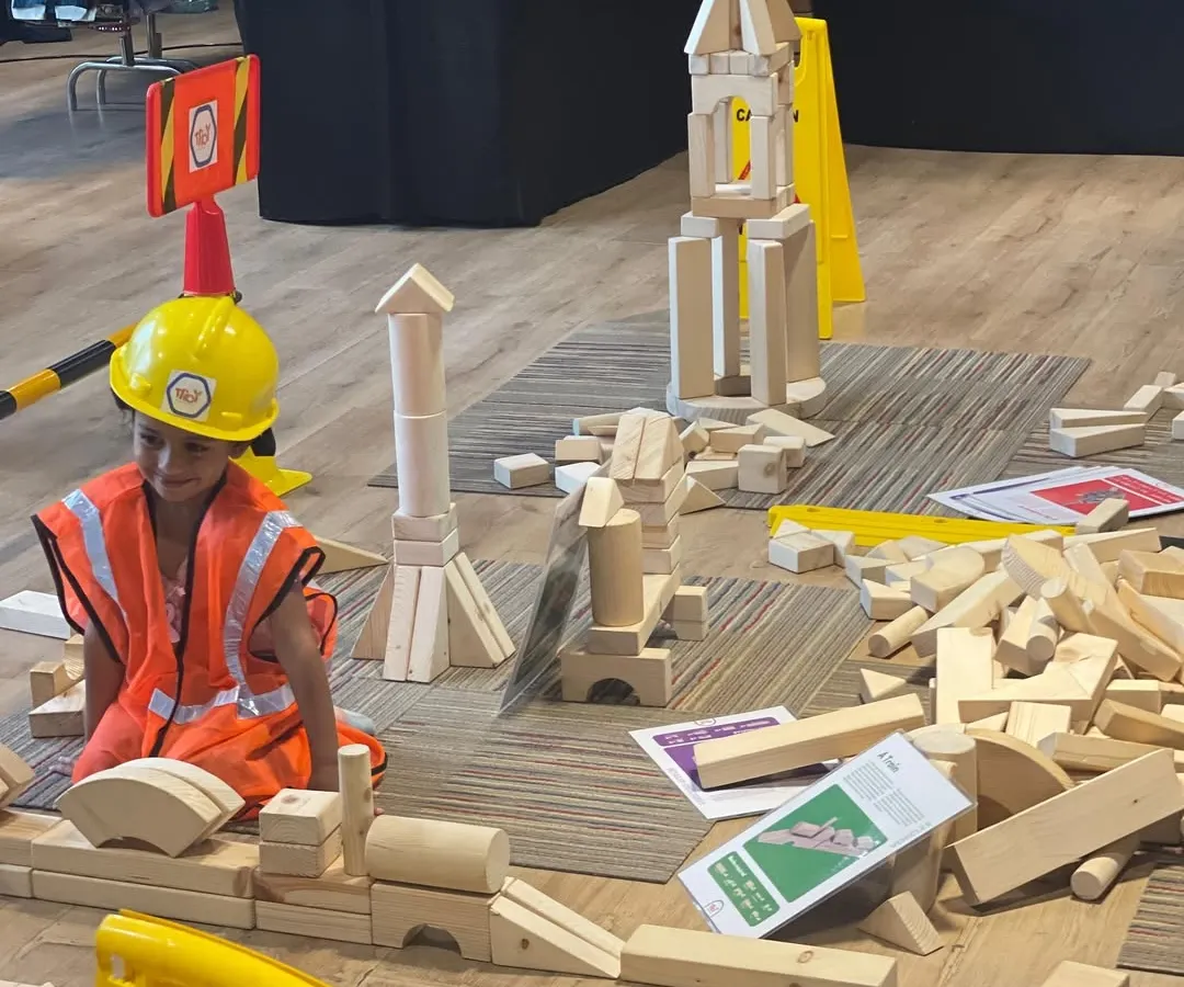 I believe in the power of play, and our dedicated kids' zones are designed for exactly that. Here, a young engineer is completely absorbed in building with giant wooden blocks, an example of the open-ended, creative fun I arrange to keep your children happily engaged.