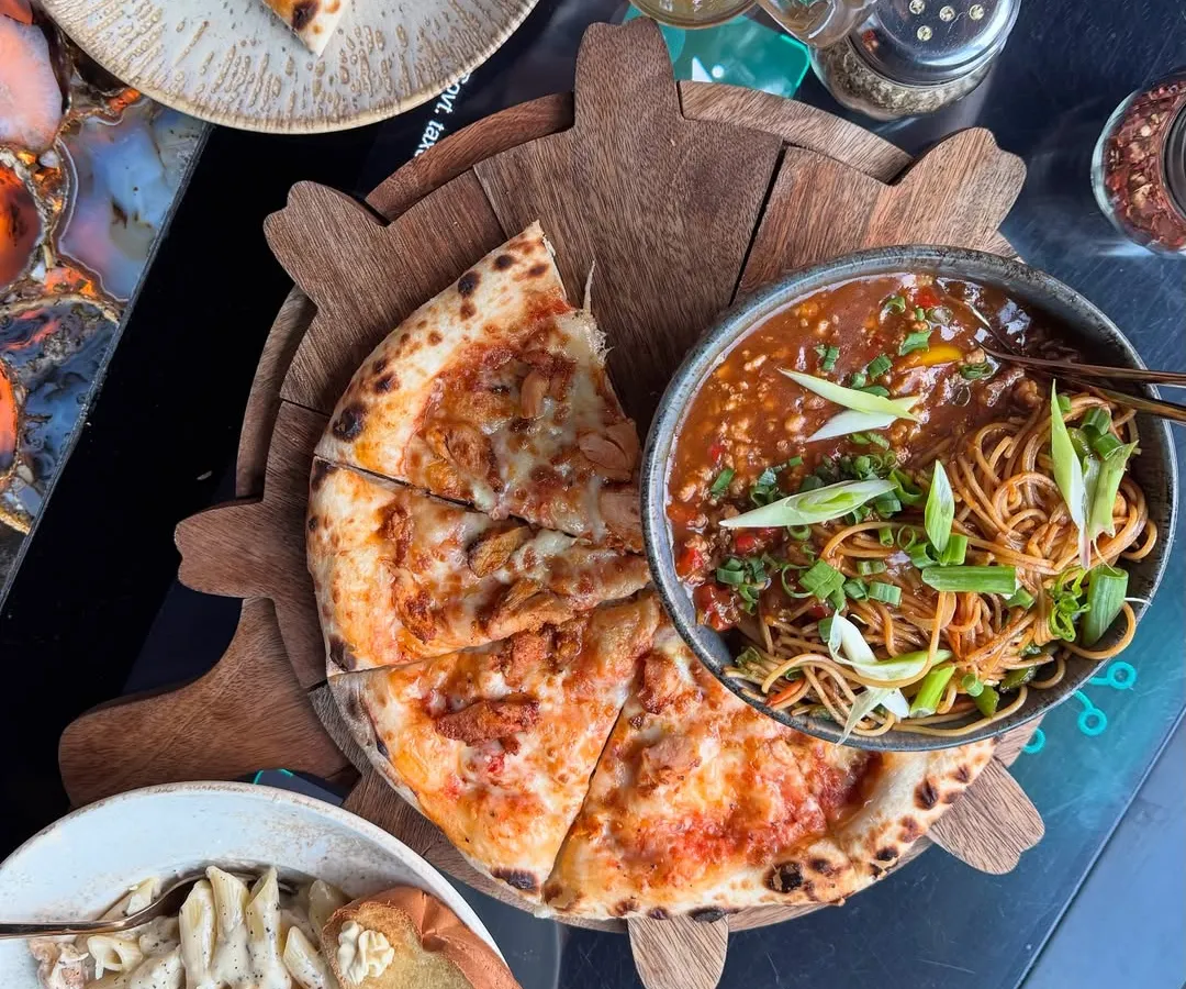 A perfect flat lay showcasing a delicious spread at a trendy Noida cafe. I focus on making the food look as good as it tastes, capturing everything from wood-fired pizza and savory noodles to creamy pasta, encouraging my audience to save the spot for their next meal.
