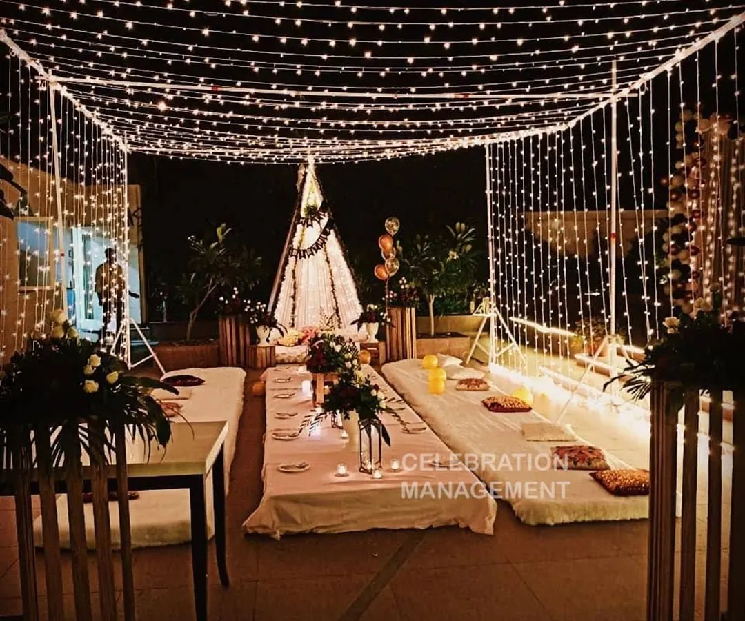 I can turn any terrace into a magical setting for a birthday dinner. This setup features a canopy of fairy lights creating a starry sky effect, with low seating on mattresses and cushions for a cozy, intimate gathering with friends and family.