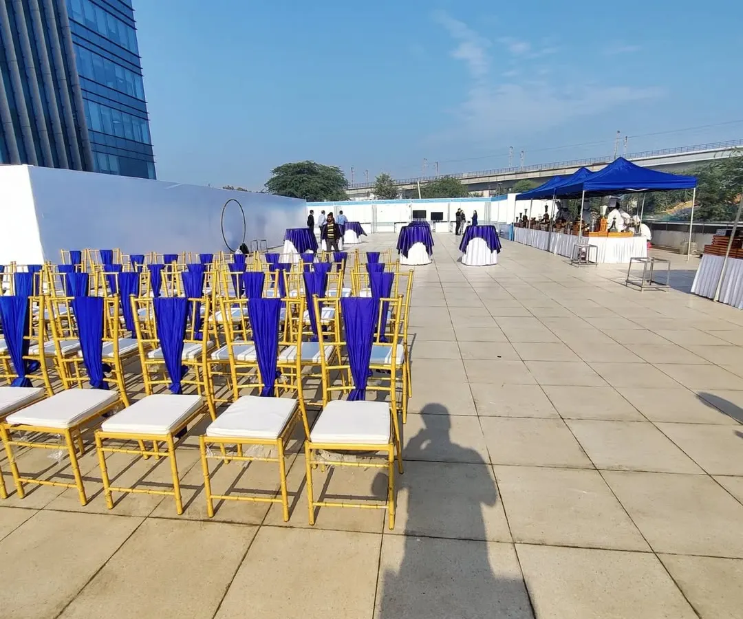 For corporate clients like Indigo Airlines, we execute professional outdoor events with precision. This rooftop setup features neatly arranged Chiavari chairs with custom blue fabric, reflecting the company's branding against a clean, urban backdrop.