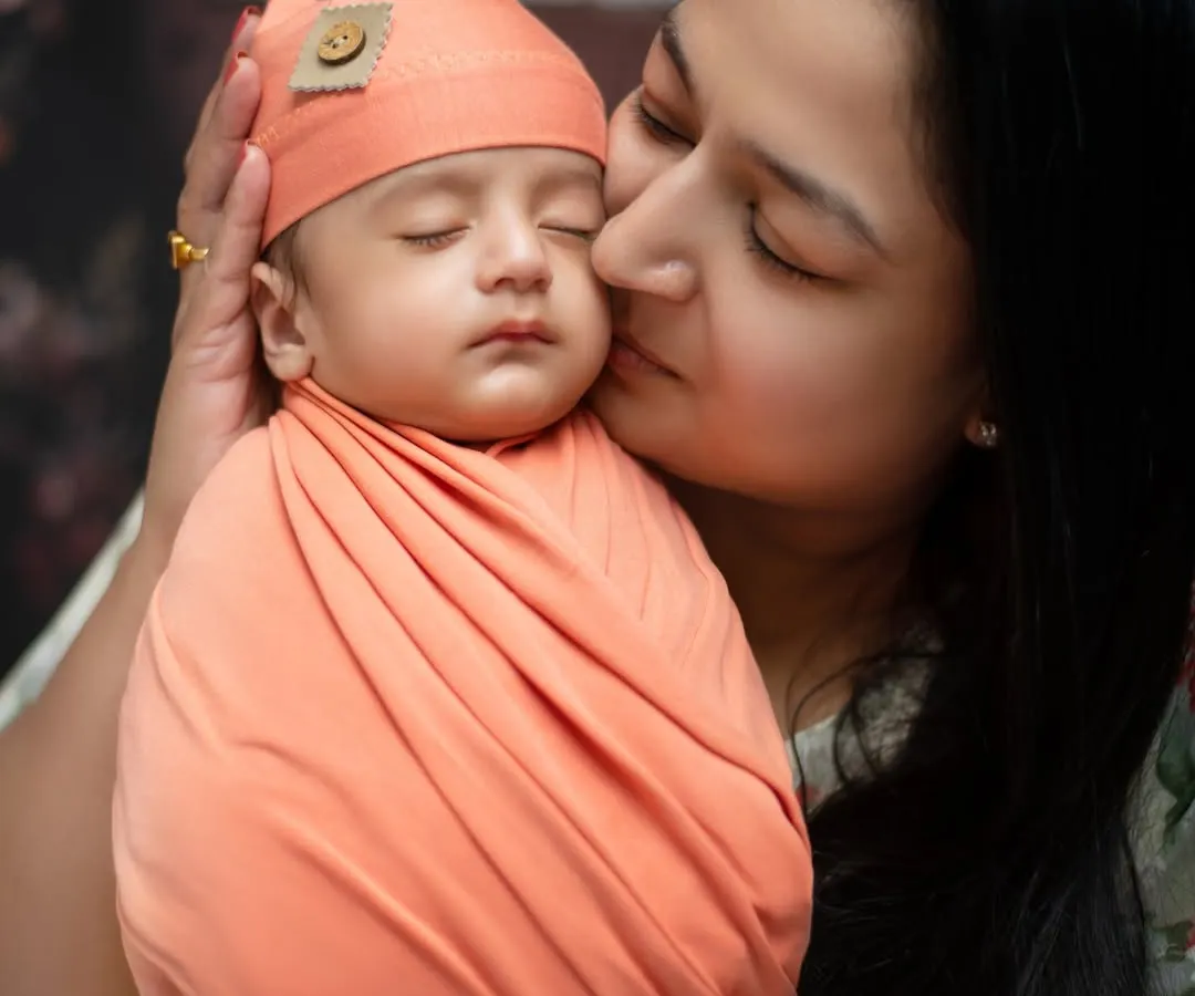 A mother’s gentle kiss for her sleeping newborn. Our specialized newborn sessions focus on creating these quiet, precious moments, using soft wraps and props to ensure your baby is safe and comfortable.
