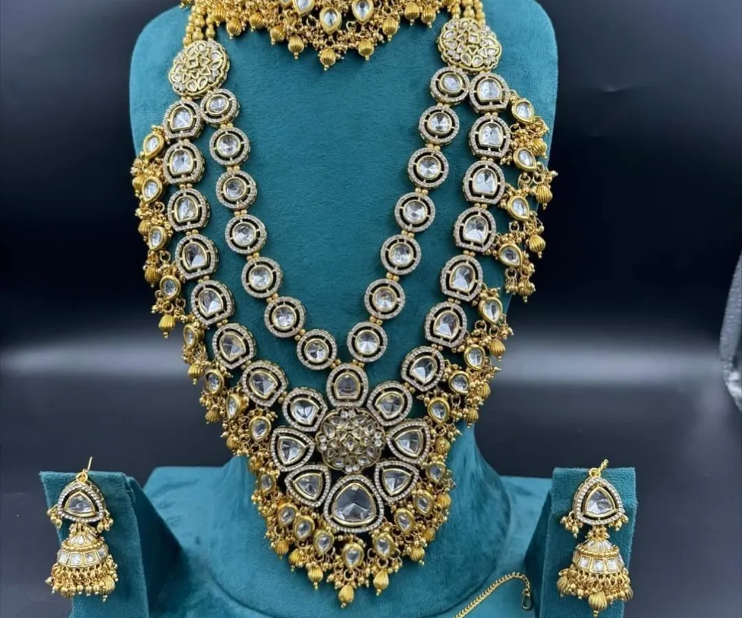 This is one of our grandest bridal sets, perfect for making a statement. It features multiple layers of American diamonds and Kundan work, including a heavy choker, a three-layer rani haar, matching jhumkas, and a maang tikka. It gives you a luxurious designer look at an affordable rental price.