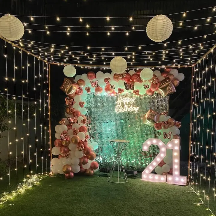 Celebrating a 21st birthday with a glamorous terrace decoration. This setup features a sparkling shimmer wall, a neon 'Happy Birthday' sign, marquee numbers, and a canopy of fairy lights to create a stunning nighttime ambiance.