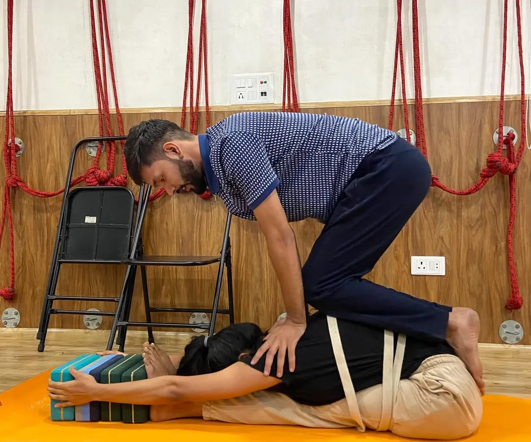I believe in a hands-on approach to ensure you are safe and getting the most out of every posture. Here, I'm assisting a student in a supported forward bend, using a chair, blocks, and straps to deepen the stretch without any strain on the back.