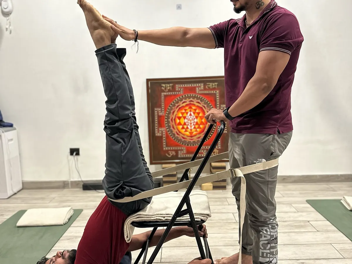 This is a supported shoulder stand, or Sarvangasana, using a chair and belts. This therapeutic setup ensures correct alignment, decompresses the spine, and allows the practitioner to receive the full benefits of the inversion safely. In my training, you will master the art of using props to make yoga accessible and beneficial for every body.
