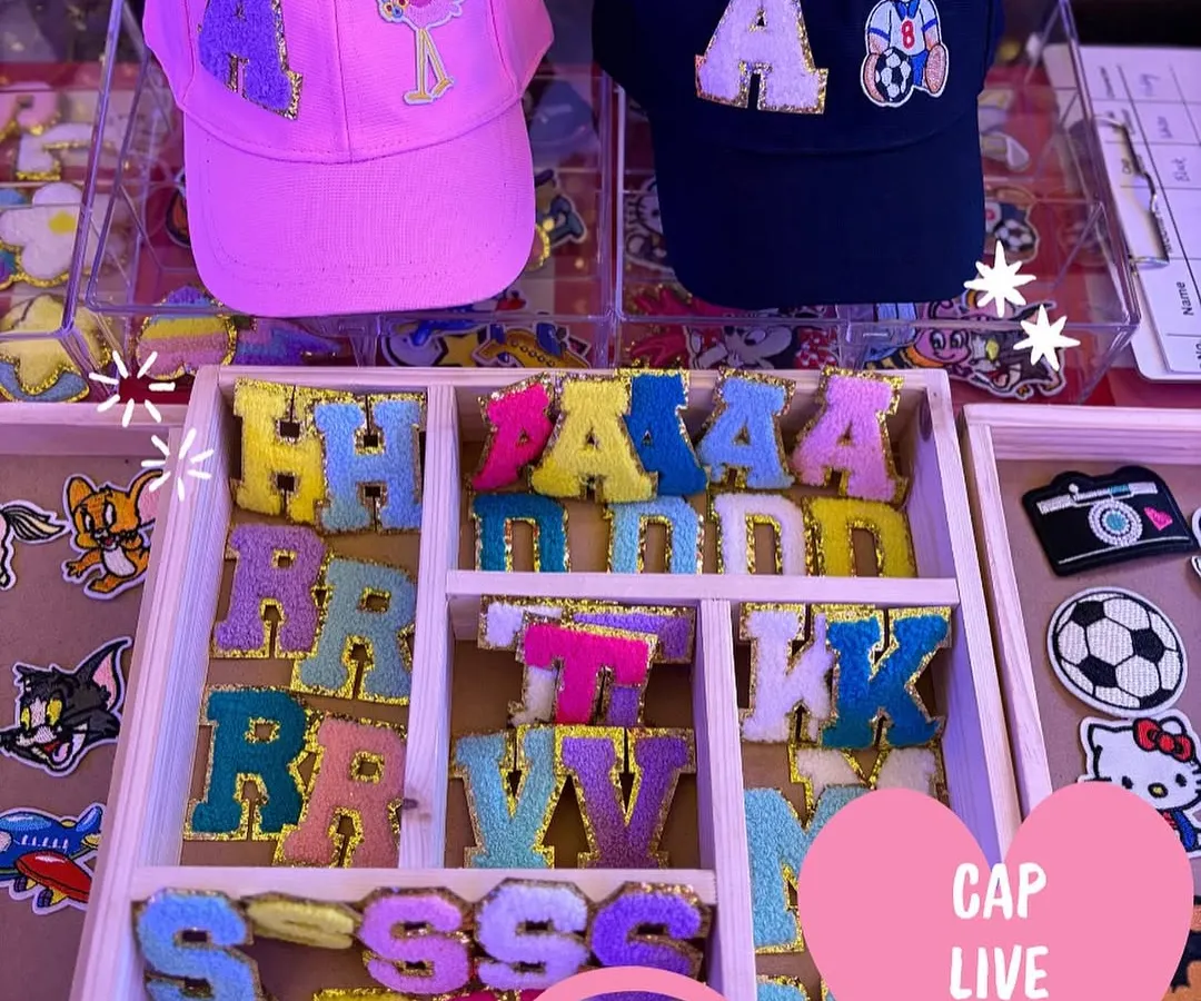 A glimpse of our live cap customization station, showing a variety of colorful chenille initial patches and character designs ready for guests to choose from. This is where the creative fun begins at your event.