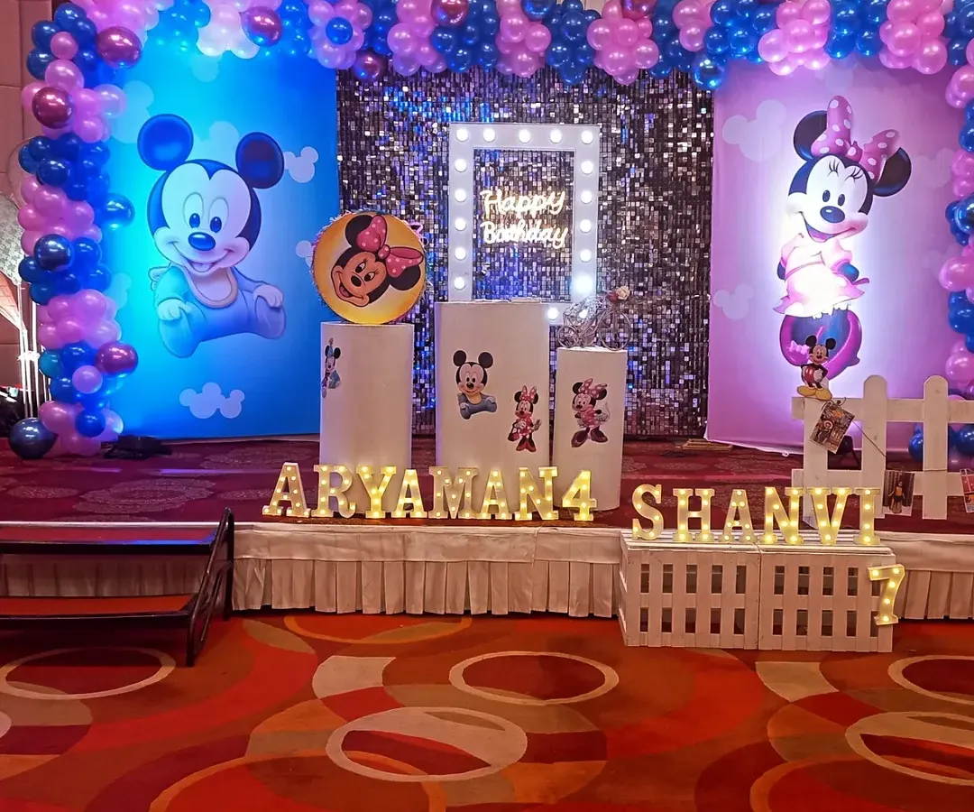 This is a complete stage setup for a Mickey and Minnie Mouse themed birthday party. We included character backdrops, a central sequin panel with a "Happy Birthday" light box, and personalized light-up names for the birthday kids, Aryaman and Shanvi.