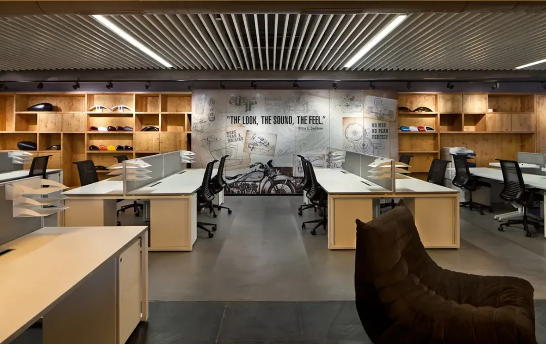 For the Harley-Davidson workspace, we translated the brand's iconic identity into a physical environment. This open-plan office features a custom mural with the tagline "The Look, The Sound, The Feel," surrounded by raw, industrial materials and displays of motorcycle parts, creating a space that authentically reflects the company's culture.