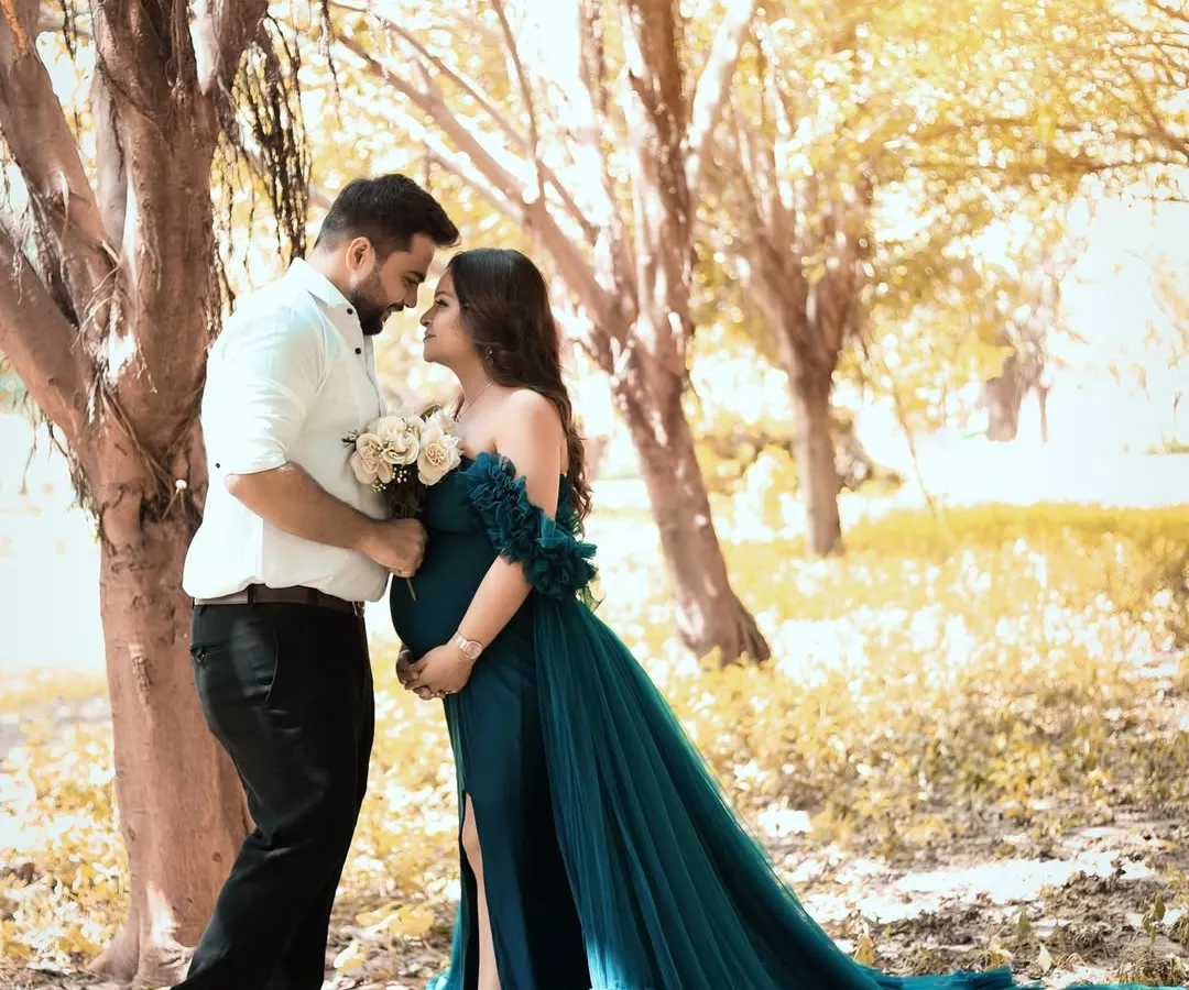 A romantic outdoor maternity portrait of a couple, bathed in the soft golden hour light. The way her teal gown flows in the gentle breeze adds a touch of fairytale magic to their special moment.