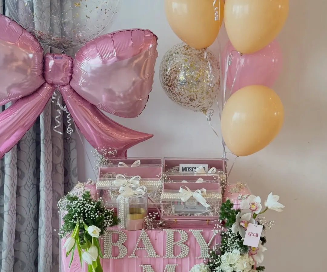 Welcoming a baby girl with all the elegance she deserves. This stunning acrylic hamper features personalized pearl lettering, designer gifts, and a cascade of fresh flowers, all tied together with a beautiful pink bow.