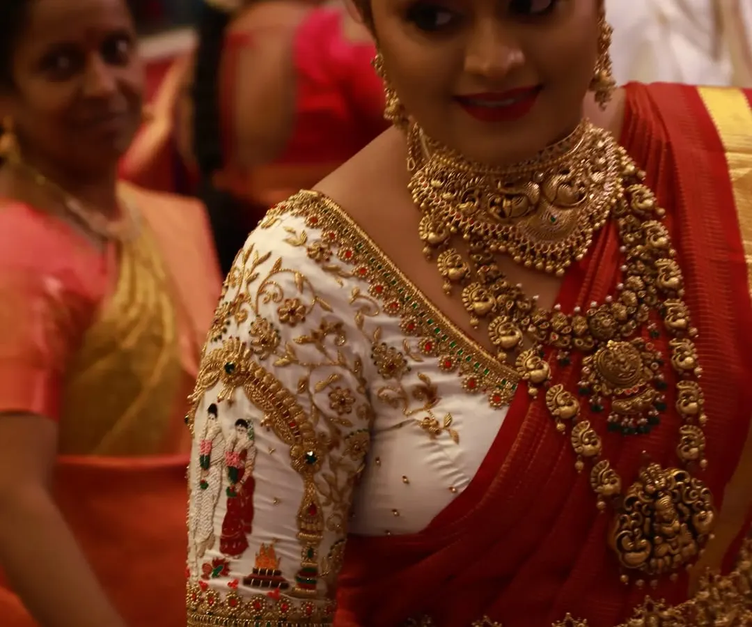 Seeing a bride's happiness is the best part of my work. Here is a client looking radiant on her wedding day in a custom white and red blouse, featuring intricate bride and groom figures embroidered on the sleeves.