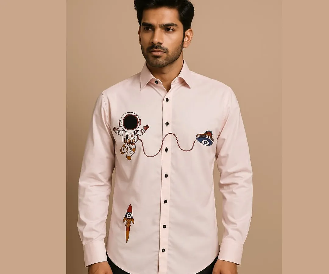 Showcasing a playful side, this light pink bespoke shirt is detailed with quirky, colorful hand embroidery of an astronaut and rocket. The design adds a touch of personality to a classic button-down, perfect for a smart casual look.