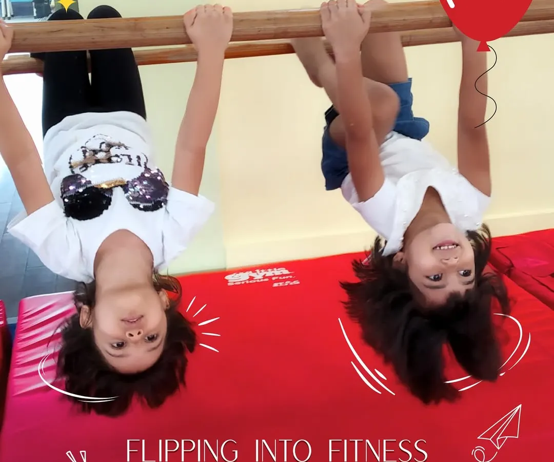 Flipping into fitness is all about smiles and support. Here, two friends build upper body strength and coordination on the gymnastics bar, learning that getting strong can be full of giggles.