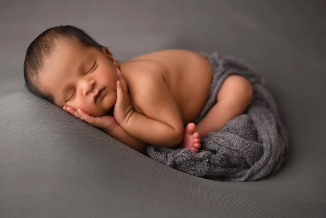 The perfect, peaceful newborn pose. As a certified newborn photographer, I ensure your baby is safe and comfortable to capture these sleepy, curled-up moments. This classic shot on a simple grey backdrop highlights the delicate features of this sweet baby boy.